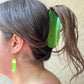 Person with a green pickle-shaped hair clip in their hair, wearing matching earrings.
