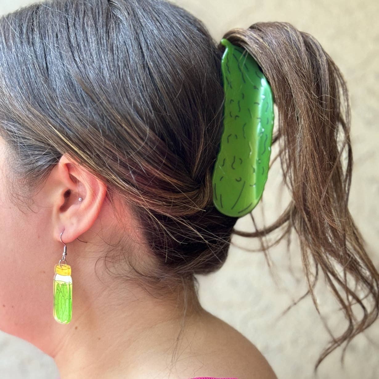 Person with a green pickle-shaped hair clip in their hair, wearing matching earrings.