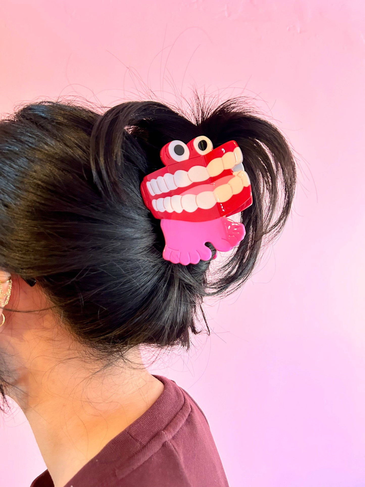Hair clip shaped like a cartoonish toothy monster on a person's hair against a pink background