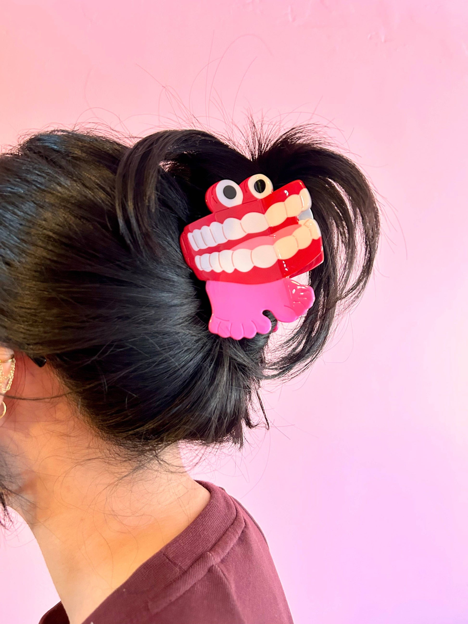 Hair clip shaped like a cartoonish toothy monster on a person's hair against a pink background