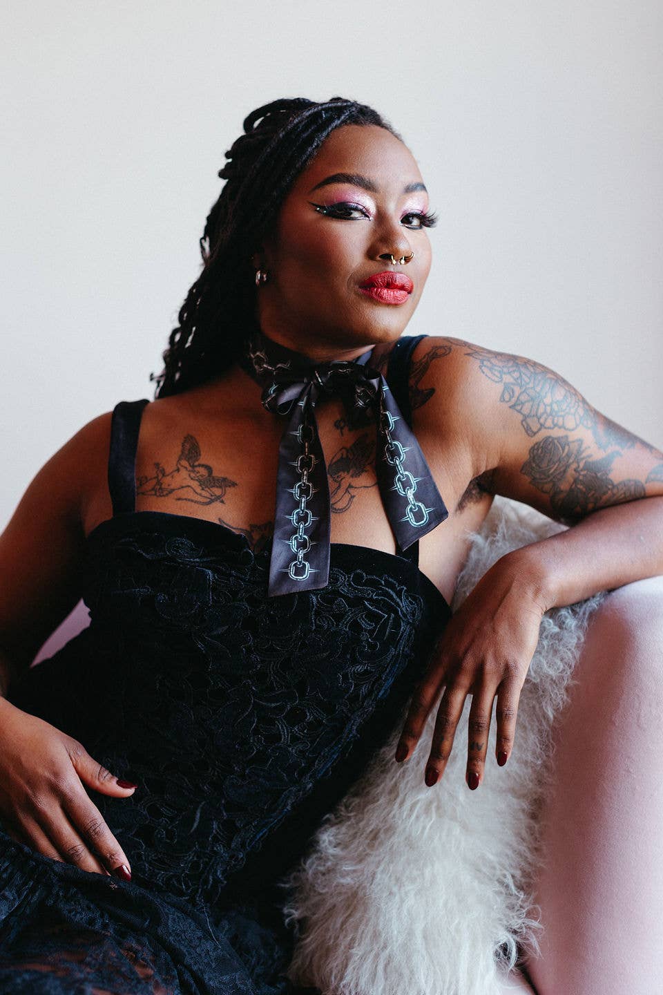 Woman in a black dress with a decorative neck piece sitting on a white surface.