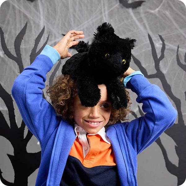 Person playing with a black cat stuffed animal against a gray background with tree silhouettes.