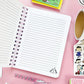 Open notebook with lined pages on a pink surface with Peanuts-themed items.
