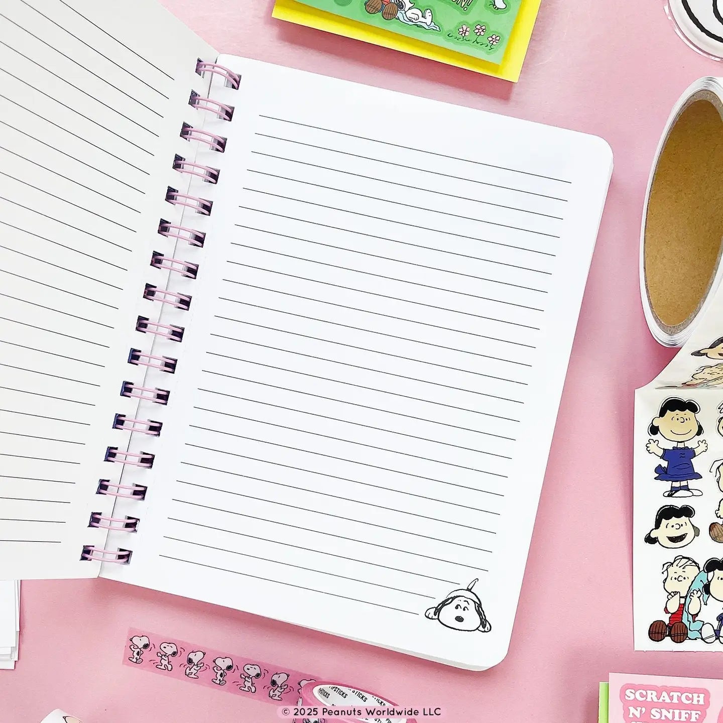 Open notebook with lined pages on a pink surface with Peanuts-themed items.