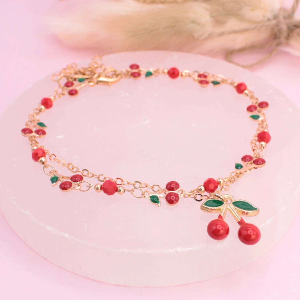 Bracelet with red and green cherry beads on a pink surface