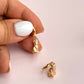 Gold cat hoop earrings held between fingers against a light pink background