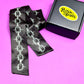 Black satin scarf with chain design next to a box labeled 'Peach Beast' on a pink background