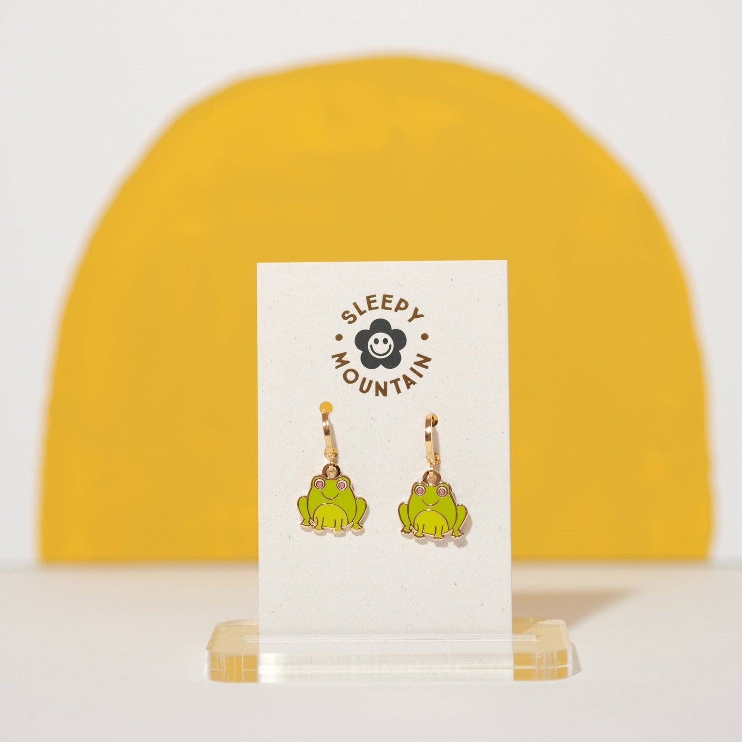 Frog-shaped earrings on a display card with 'Sleepy Mountain' branding against a yellow and white background.