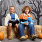 Two children sitting on hay bales with Halloween decorations, including pumpkins and spider webs.