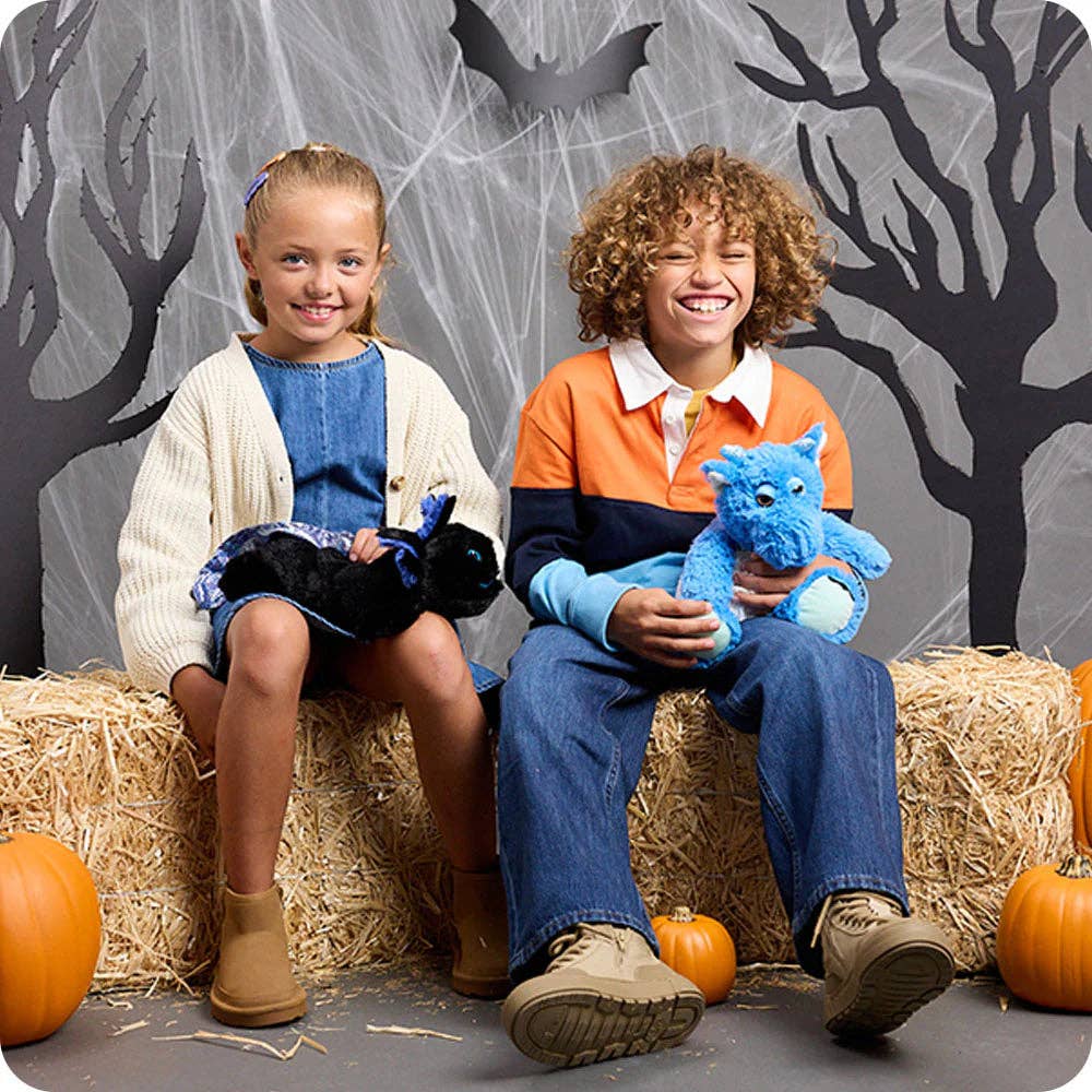 Two children sitting on hay bales with Halloween decorations, including pumpkins and spider webs.