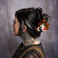 Person with tattoos and colorful hair accessory against a gray background