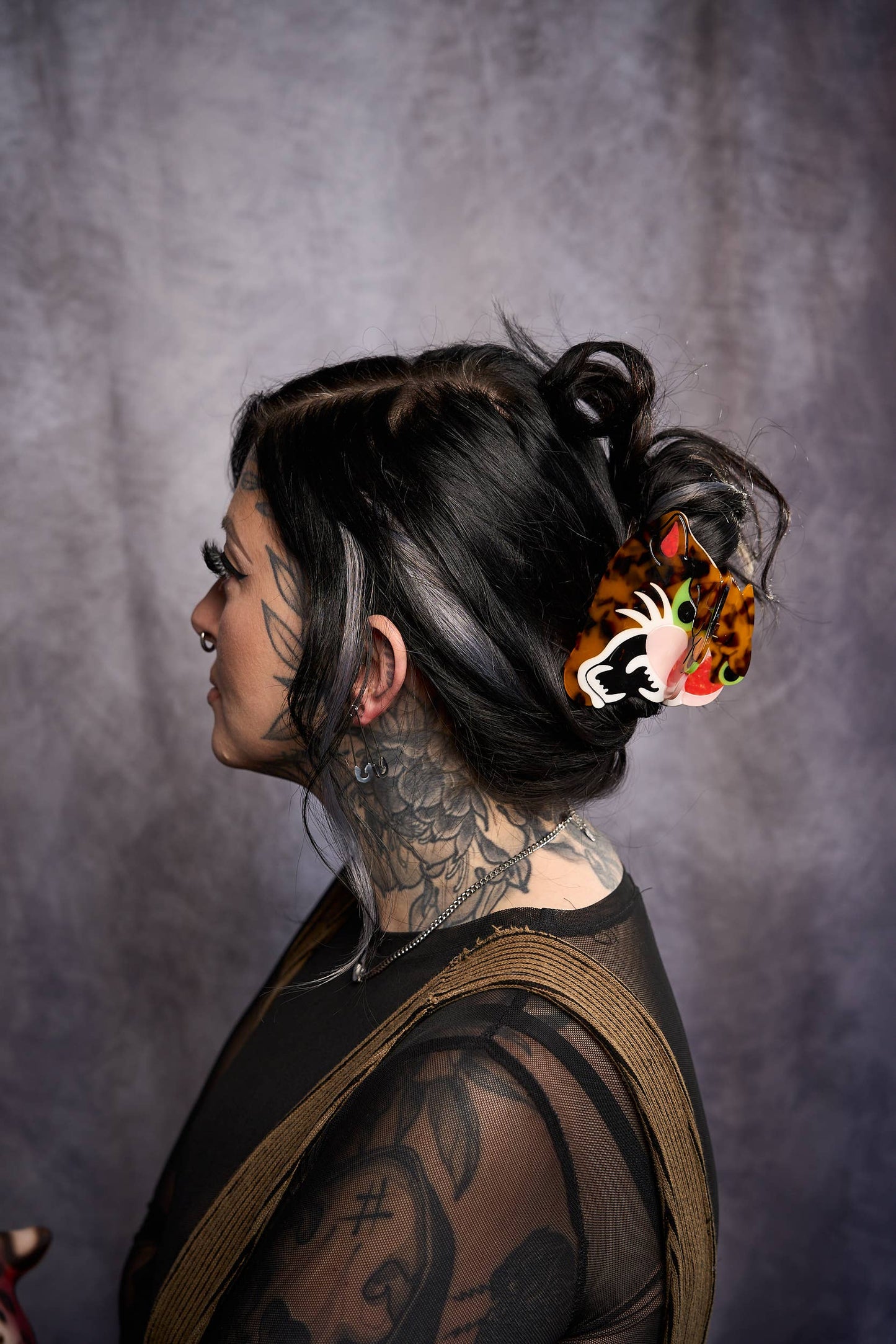 Person with tattoos and colorful hair accessory against a gray background
