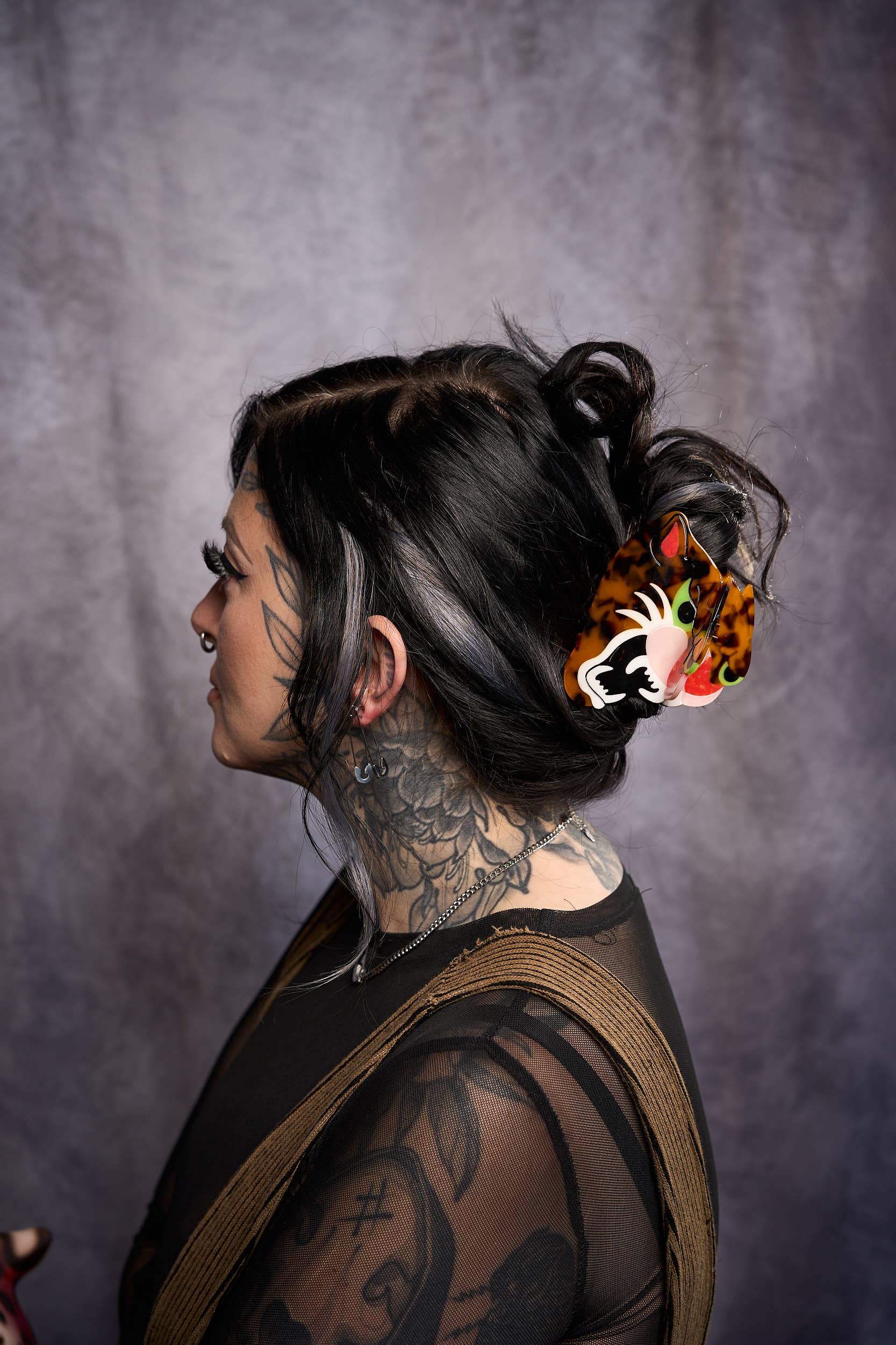 Person with tattoos and colorful hair accessory against a gray background