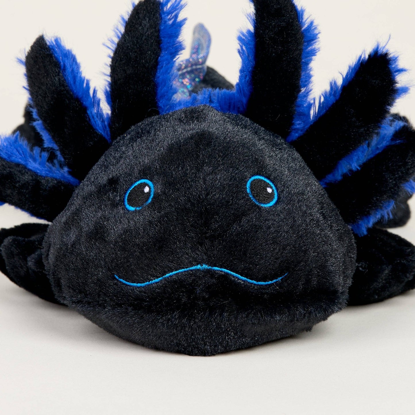 Plush toy axolotl with black body and blue spikes on a white background