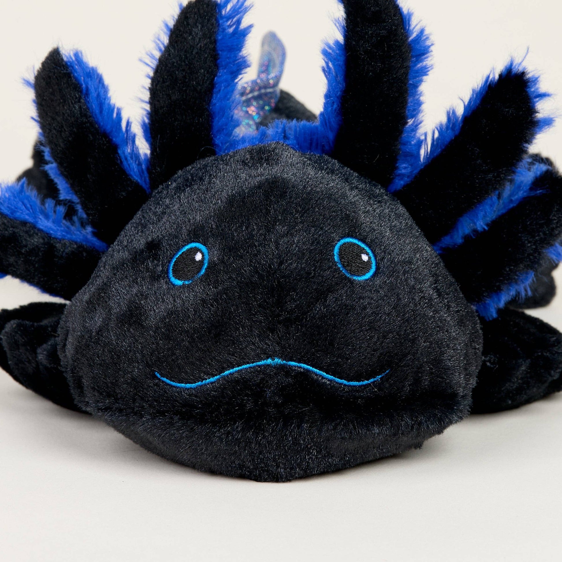 Plush toy axolotl with black body and blue spikes on a white background