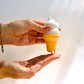 Hand holding a small ice cream cone-lotion container with white top and yellow body against a light background