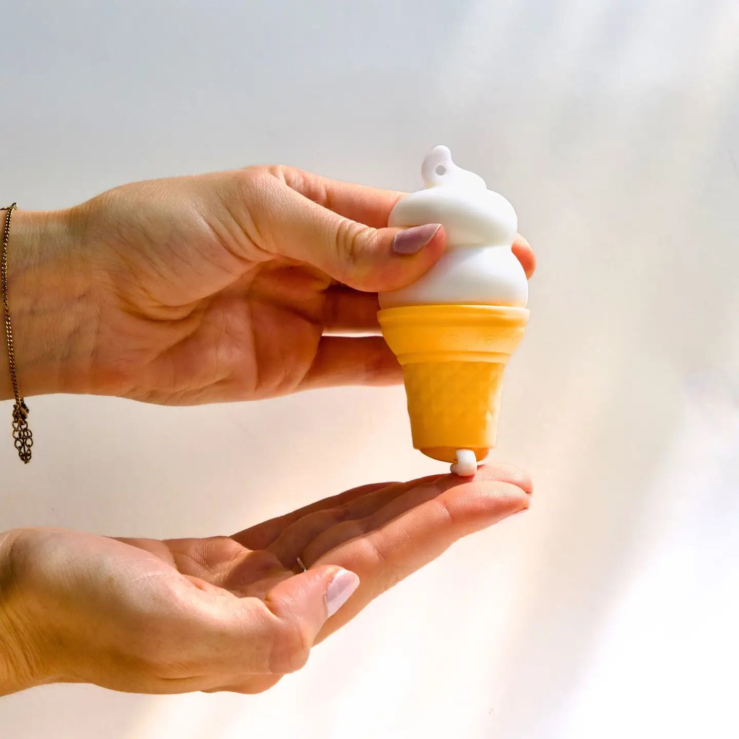 Hand holding a small ice cream cone-lotion container with white top and yellow body against a light background