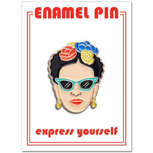 Enamel pin with a design of a woman's face wearing sunglasses and flowers in her hair, on a white background with red text.