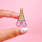 Hand holding a colorful ice cream cone-shaped pin against a pink background