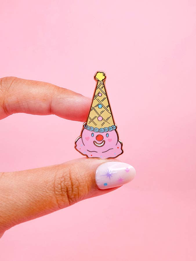 Hand holding a colorful ice cream cone-shaped pin against a pink background