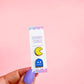 Hand holding a card with two colorful Pac-Man ghost pins against a pink background