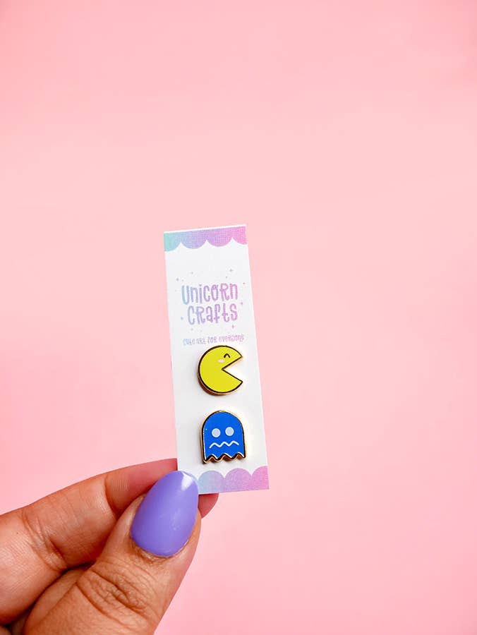 Hand holding a card with two colorful Pac-Man ghost pins against a pink background