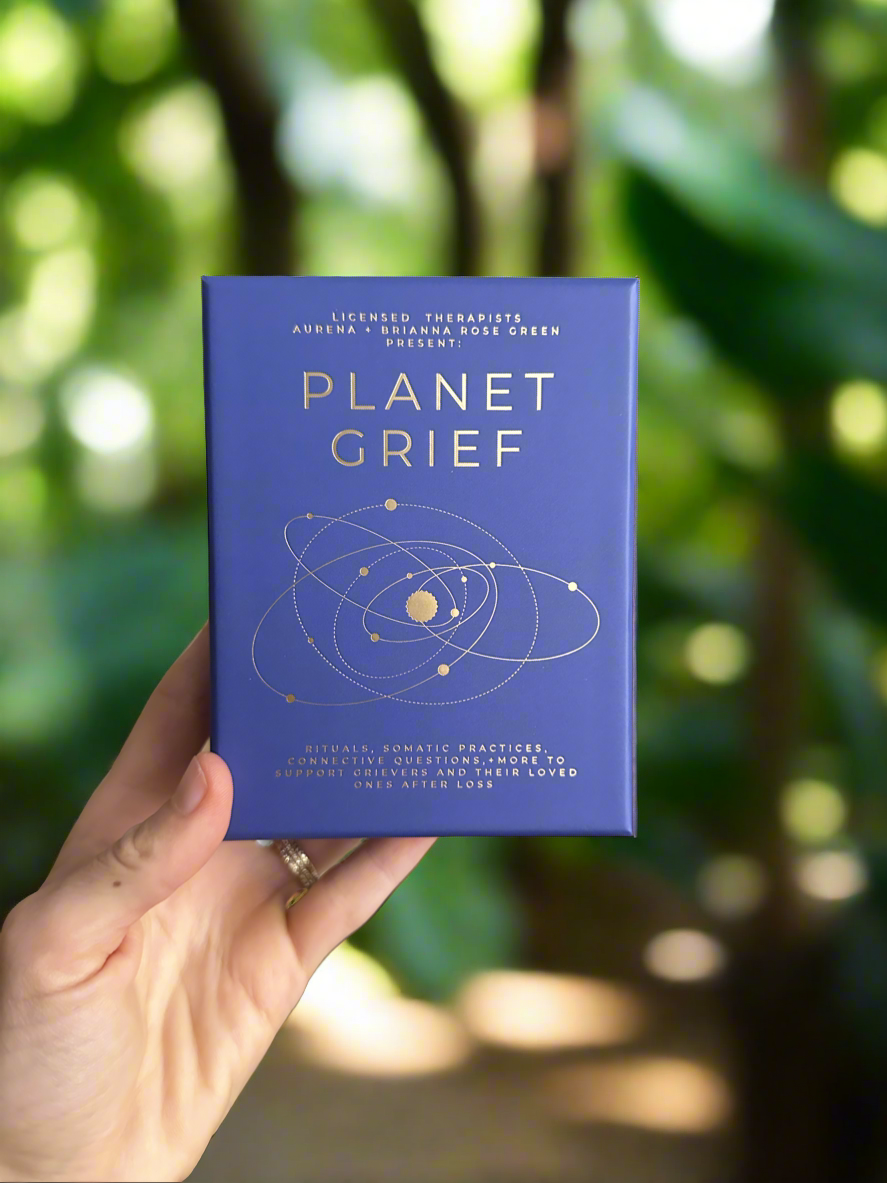 Hand holding a blue book titled 'Planet Grief' against a blurred natural background