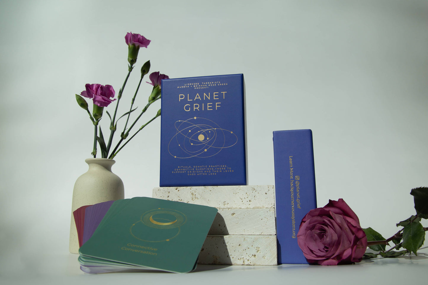 Books titled 'Planet Grief' and 'The Book of Shadows' with flowers on a white surface.