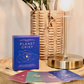 Card deck titled 'Planet Grief' on a wooden surface with a lamp and plant in the background.
