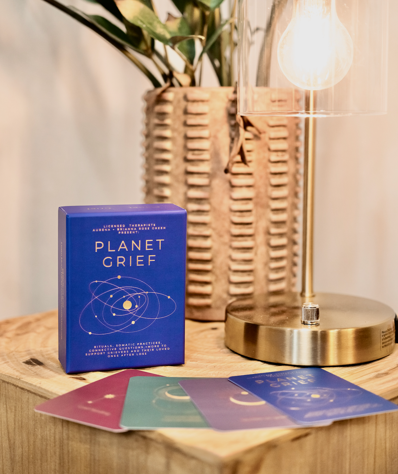 Card deck titled 'Planet Grief' on a wooden surface with a lamp and plant in the background.