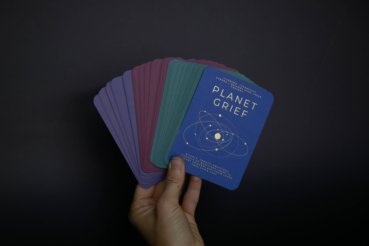 Hand holding a deck of cards titled 'Planet Grief' against a dark background