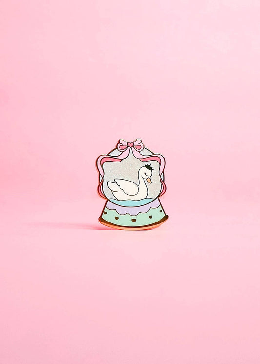 Decorative pin with a swan design on a pink background
